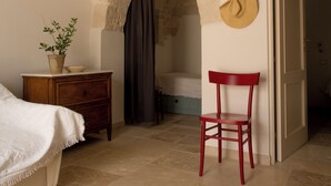 Un dormitorio con un arco de piedra, una cama, una mesita de noche, una silla y una puerta que da a otra habitación.
