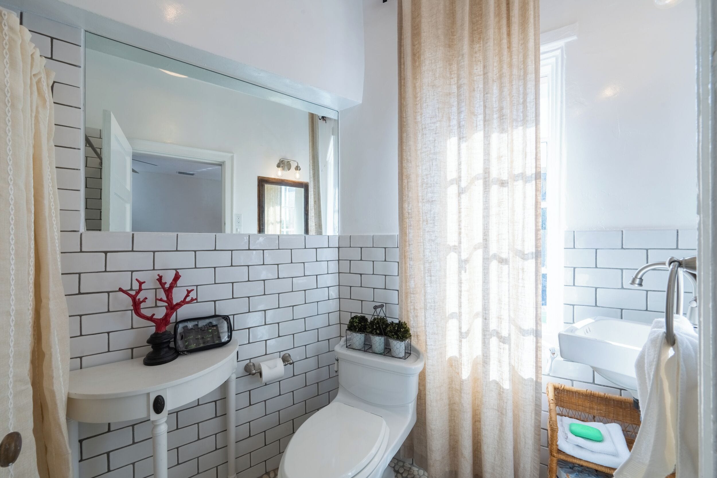 A bathroom with white tiled walls, a white sink, a toilet, and a mirror above the sink.
