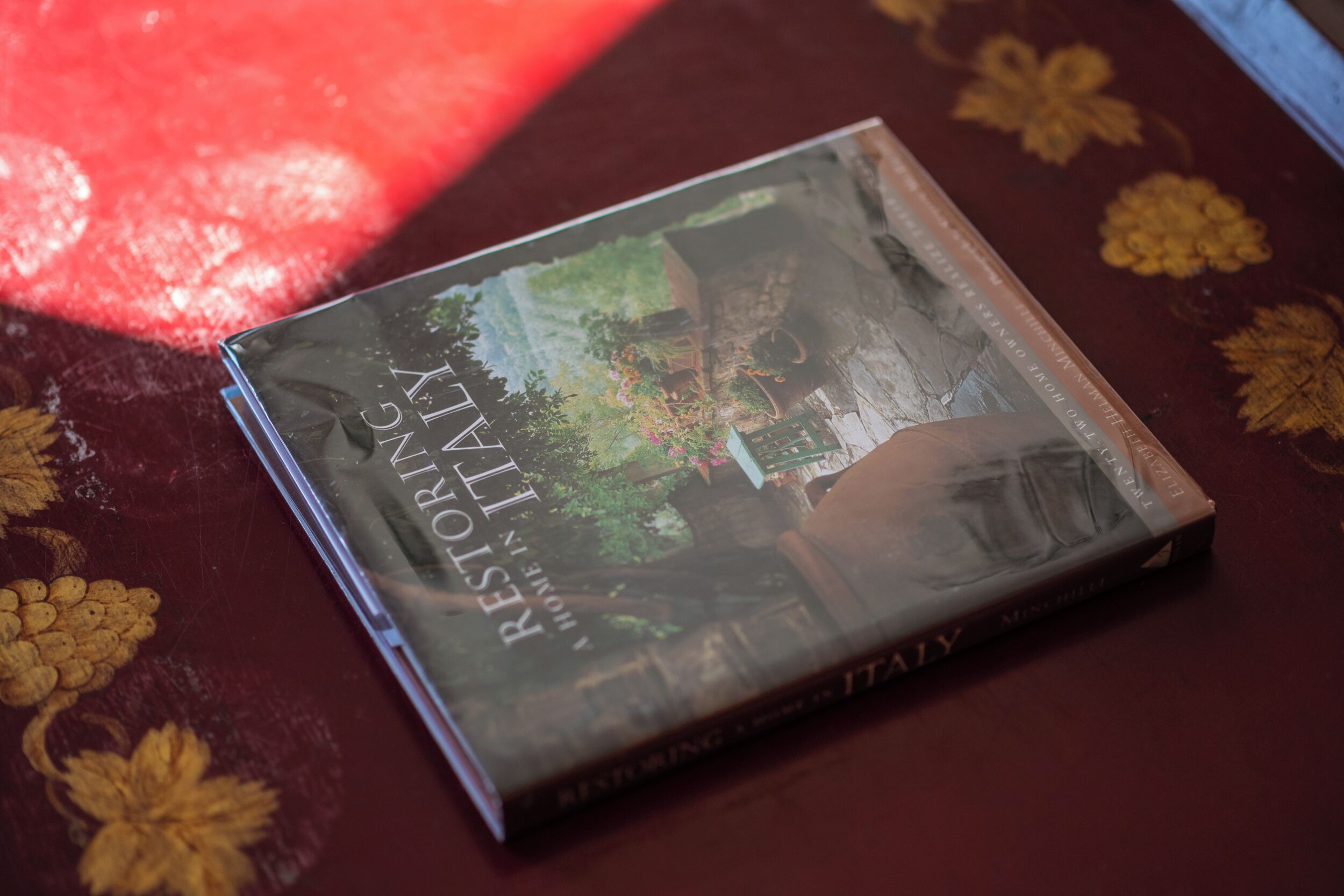 Een boek met de titel 'Restoring Italy' op een tafel met een bloemenprint.