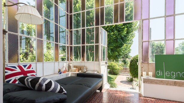 Une pièce moderne avec un canapé noir, une lampe et une vue sur la verdure grâce à de grandes fenêtres.
