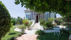 Une maison avec une allée dallée, un petit jardin agrémenté d’une table et de chaises, et un chemin menant à la porte.