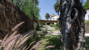 Un chemin de pierres mène à une maison, près d’un grand tronc d’arbre et d’une clôture en métal.