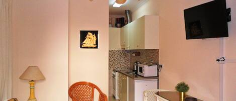 A compact living space with a kitchenette, a dining area with a table and chairs, a sofa, and a decorative lamp.