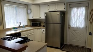 A compact kitchen with white cabinets, a stainless steel refrigerator, a microwave, and a gas stove.