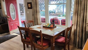 A dining area with a wooden table, four chairs, and a window with a view of red chairs outside.