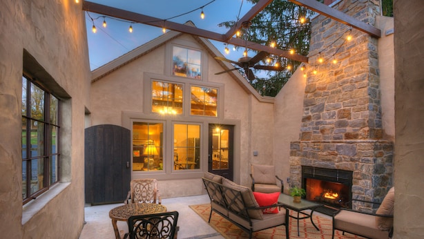 Un espace patio accueillant avec une cheminée en pierre, des sièges d’extérieur et des guirlandes lumineuses.