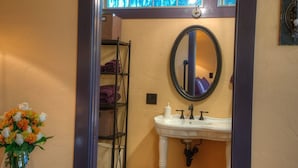 Une salle de bain avec un lavabo blanc, un miroir rond et un vase de fleurs.