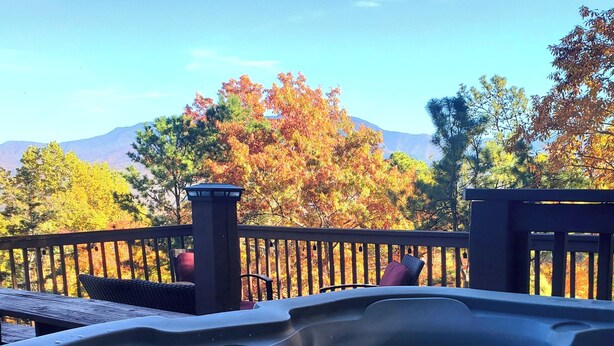 Un jacuzzi con terraza de madera y vistas a árboles otoñales y montañas.