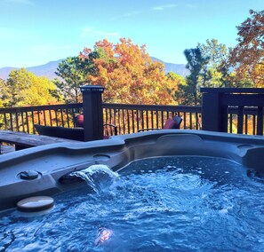 Un jacuzzi con terraza de madera y vistas a árboles otoñales y montañas.