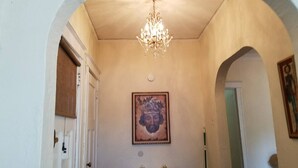 Un passadís amb un lampadari, un quadre amb marc a la paret i una porta a l'esquerra.