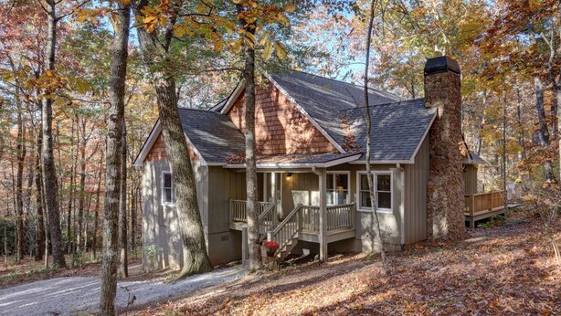 A cabin with a stone chimney, a porch, and a staircase leading to a deck.