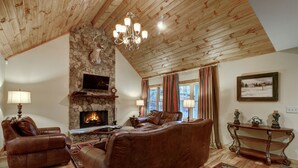 A cozy living room with a stone fireplace, leather furniture, and a chandelier.