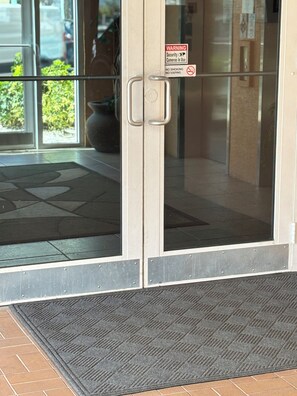 A glass door with a security warning sign, a metal handle, and a doormat.