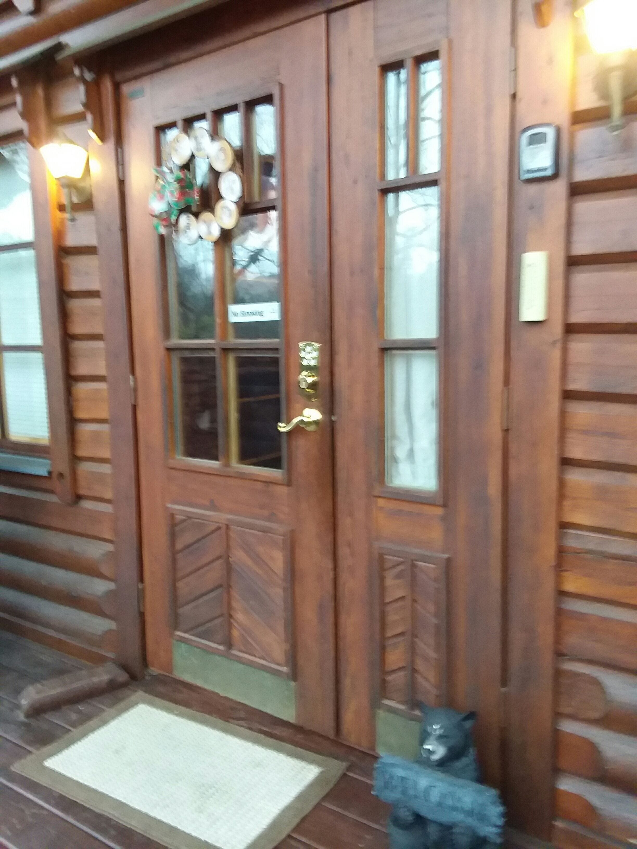 Entrada de una cabaña de madera con una puerta de vidrio, un felpudo y una pequeña estatua de un oso.