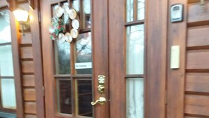 Entrada de una cabaña de madera con una puerta de vidrio, un felpudo y una pequeña estatua de un oso.