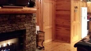 Interior acogedor de una cabaña con chimenea de piedra, paredes de madera, una estatua de oso y un televisor montado sobre la chimenea.