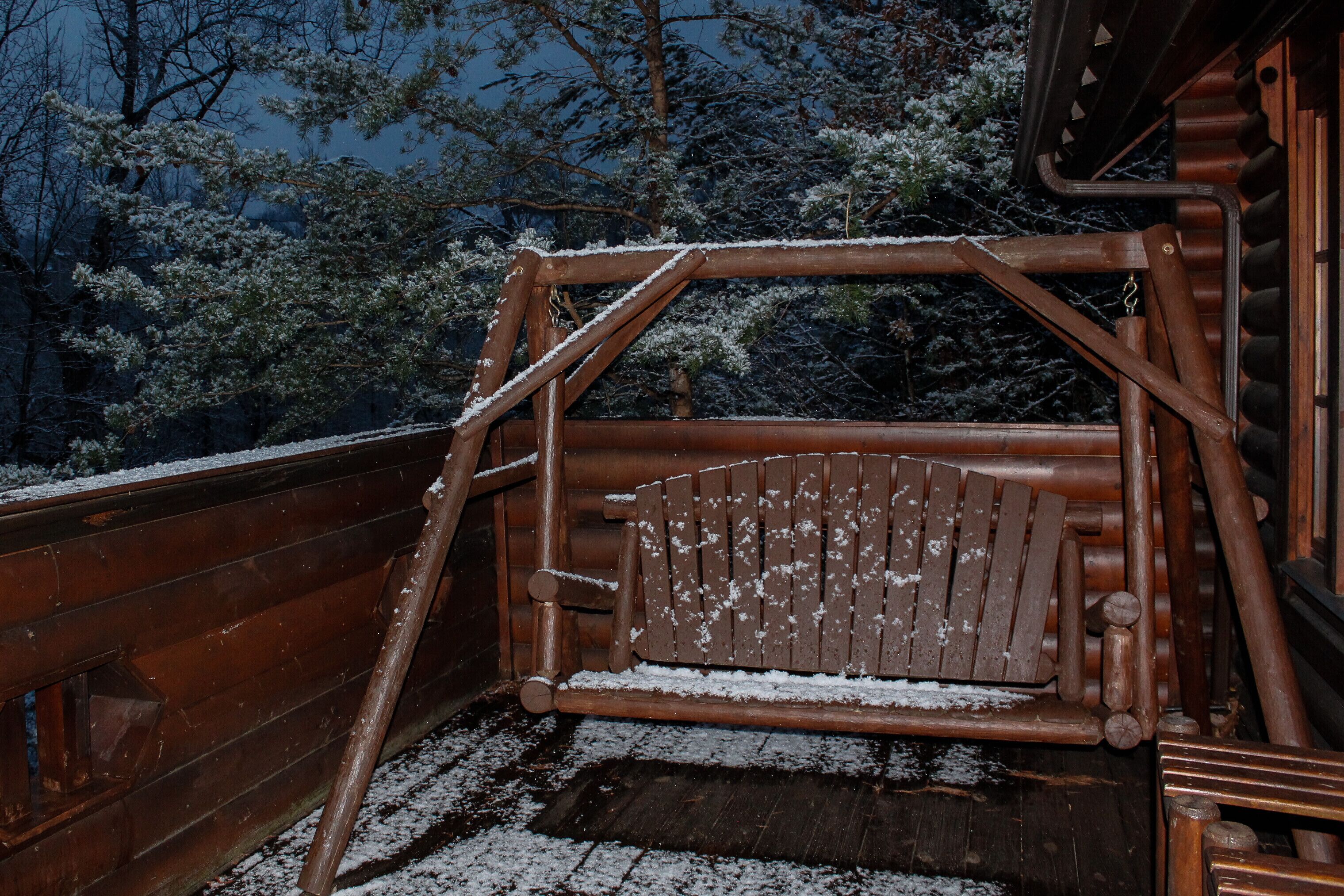 A wooden swing set with snow on the ground and surrounding trees.