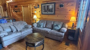 Interior acogedor de una cabaña de madera con un sofá gris, una mesita redonda y techo de madera.