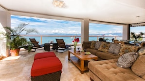 A spacious living area with a large window overlooking a scenic view, furnished with a sofa, chairs, and a coffee table. - Best location right on los muertos beach, Sky Suite E (Amapas)