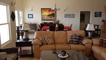 A living room with a beige sofa, a coffee table, and a dining area with a red tablecloth.