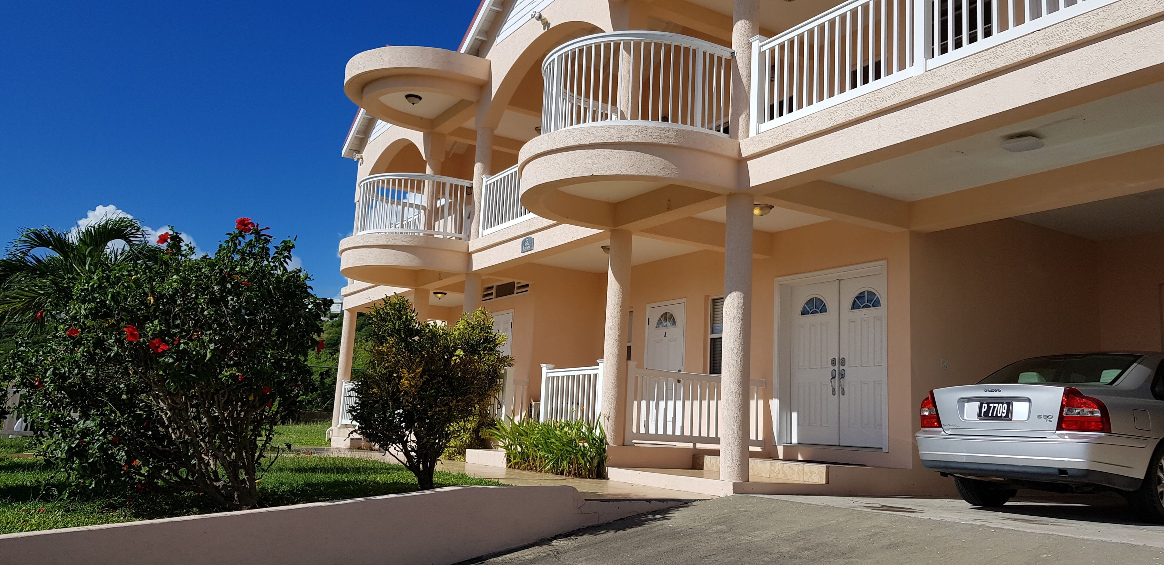 A multi-story hotel with balconies, a car parked in front, and a well-maintained garden.