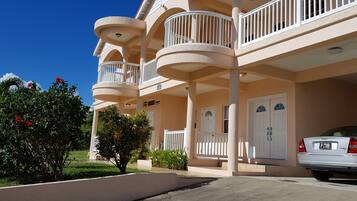 A multi-story hotel with balconies, a car parked in front, and a well-maintained garden.