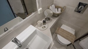A bathroom with a bathtub, sink, toilet, and a small mirror. There are toiletries and a towel rack visible. - Ermou Stylish Suite Studio (Athina)