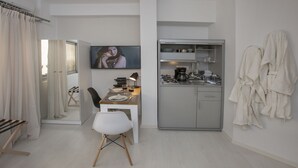 A compact hotel room with a kitchenette, a dining area with a table and chairs, a TV mounted on the wall, and a robe hanging on the wall. - Ermou Stylish Suite Studio (Athina)