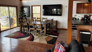 Amplia sala de estar con comedor, techo de madera, televisor grande y una cocina con armarios de madera.