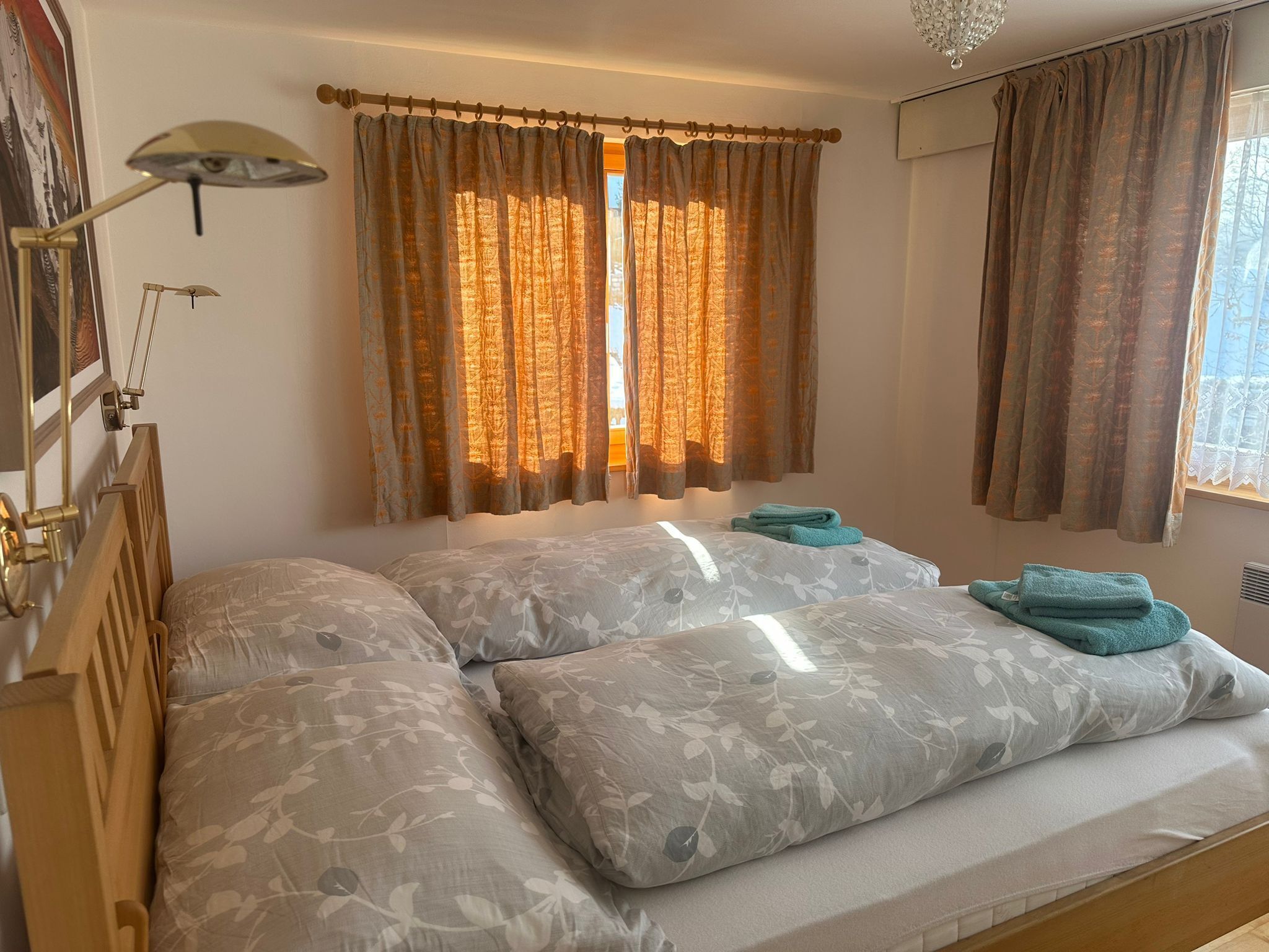 Een slaapkamer met een bed, gordijnen, een lamp en een plafondlamp.