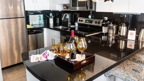Une cuisine moderne dotée d’appareils électroménagers en acier inoxydable, d’un plan de travail noir et d’un plateau sur lequel se trouvent des verres à vin et une bouteille.