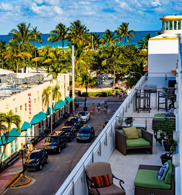 A hotel balcony with a view of the street, parked cars, and palm trees.