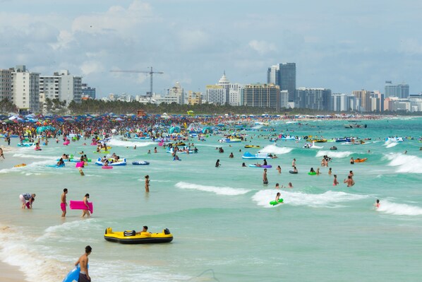 Una playa concurrida, gente nadando y usando botes inflables.