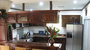 A kitchen with wooden cabinets, a stainless steel refrigerator, a bar area with wicker chairs, and a vase with flowers.