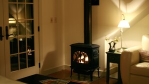 Ett mysigt rum med en vedeldad kamin, en dörr med glaspaneler, en lampa på ett bord och en stol.