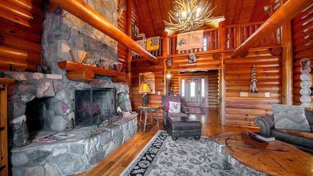 A log cabin interior with a stone fireplace, wooden beams, a chandelier, and a cozy seating area. - Lodge at Shady Branch (Hendersonville)