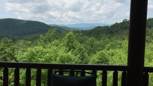 A view from a balcony with a wooden railing, overlooking a dense forest and distant mountains under a cloudy sky. - Lodge at Shady Branch (Hendersonville)