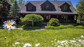 A log cabin with a porch, surrounded by well-maintained lawns and trees.