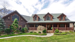 A log cabin with a large porch, multiple chimneys, and a well-maintained front yard. - Lodge at Shady Branch (Hendersonville)