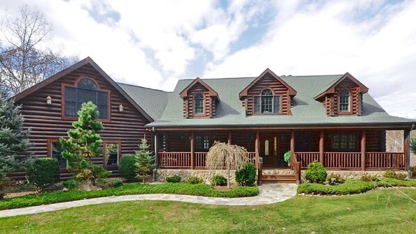 A log cabin with a large porch, multiple chimneys, and a well-maintained front yard.