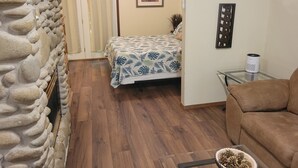 Ein Zimmer mit einem Bett, einem Sofa, einer Steinsäule, einem gerahmten Bild und einem kleinen Tisch mit einem Lautsprecher.