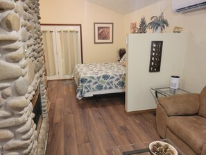 A room with a bed, a sofa, a stone wall, a framed picture, and a small table with a speaker. - 1 Bedroom Romantic Safari Hideaway - Pet Friendly - Minutes from Everything (Pigeon Forge)