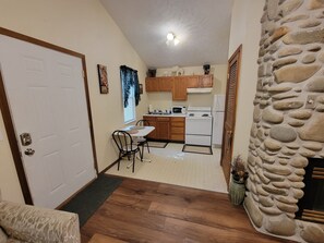 A compact kitchen with wooden cabinets, a white stove, and a dining area with a chair. - 1 Bedroom Romantic Safari Hideaway - Pet Friendly - Minutes from Everything (Pigeon Forge)