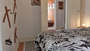 Une chambre à coucher avec un lit, une porte donnant sur une autre pièce et un mur orné d’un tableau encadré.