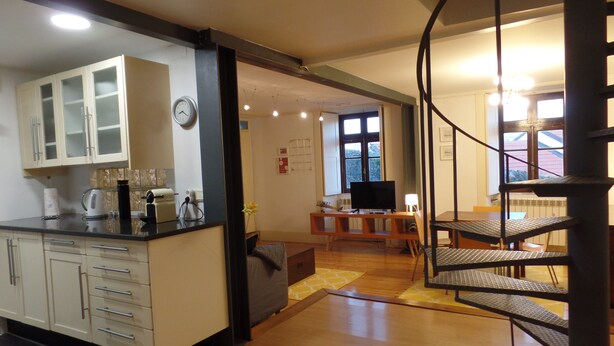 Une cuisine moderne avec des meubles blancs et un comptoir noir, un coin repas avec une table et des chaises, et un escalier en colimaçon menant à l’étage supérieur.