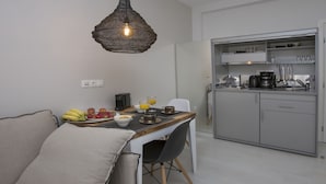 A compact kitchen with a dining area, featuring a modern pendant light, a small dining table with chairs, and a built-in kitchen cabinet with appliances. - Ermou Stylish viewing studio (Athina)