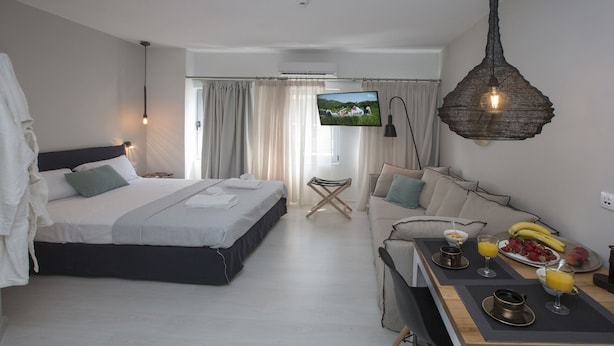 A modern hotel room with a bed, a sofa, a dining area with breakfast items, and a TV on the wall. - Ermou Stylish viewing studio (Athina)