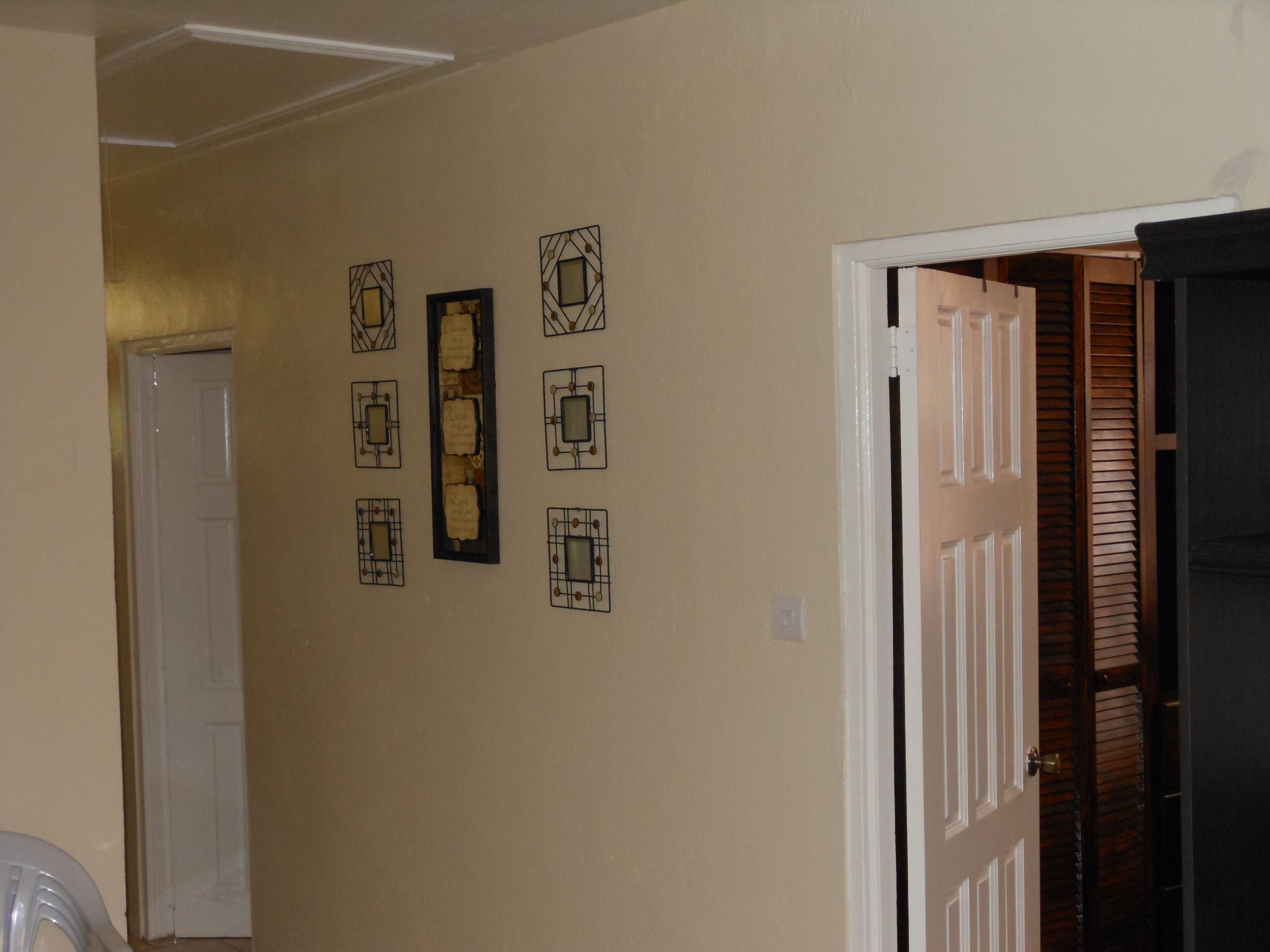 A hallway with beige walls, a white door, and a black door leading to a closet. There are six framed pictures on the wall.