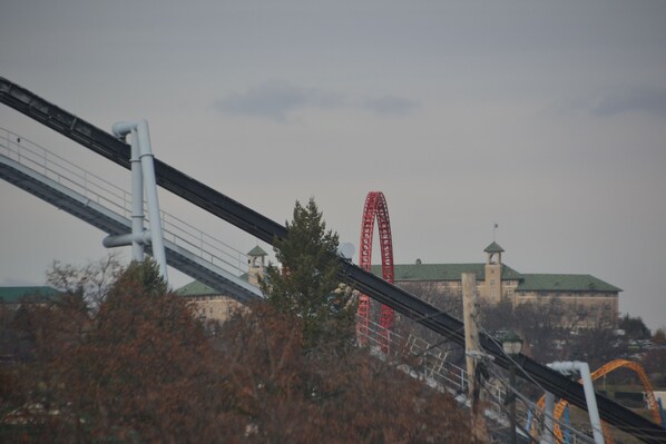 A roller coaster with a red track, a building with a green roof, and a bridge with a white structure.