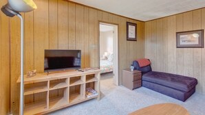 A room with wooden panel walls, a television on a wooden stand, a sofa, a small table, and a lamp.